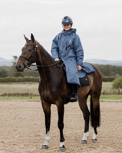 Woman in EQUIDRY Steel Blue Waterproof Horse Riding Coat on Horseback. Equestrian Apparel.