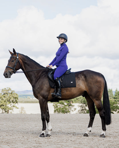 Equestrian in purple EQUIDRY water-repellent leggings on horseback. Full seat for secure horseback riding.