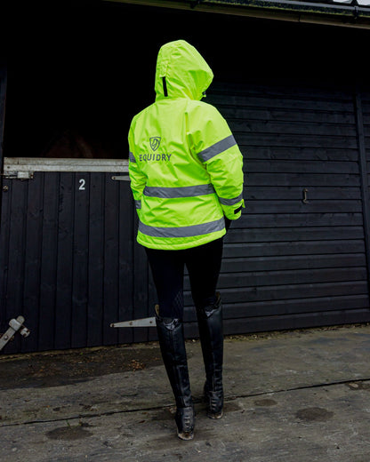 Equidry women's hi-vis yellow fleece riding coat with reflective strips, standing by a stable.