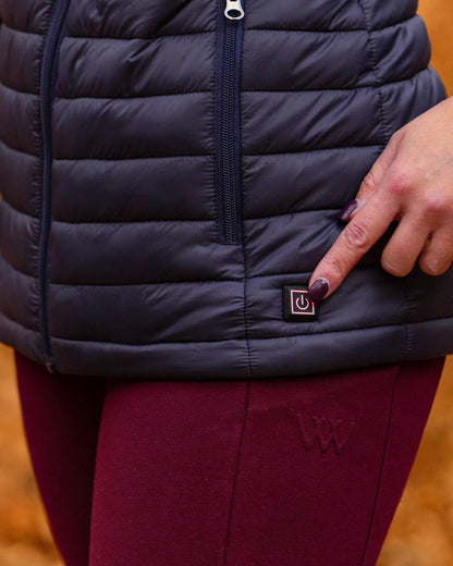 WOOF WEAR Heated Gilet Navy - Woman pressing power button on heated riding vest for core body warmth.