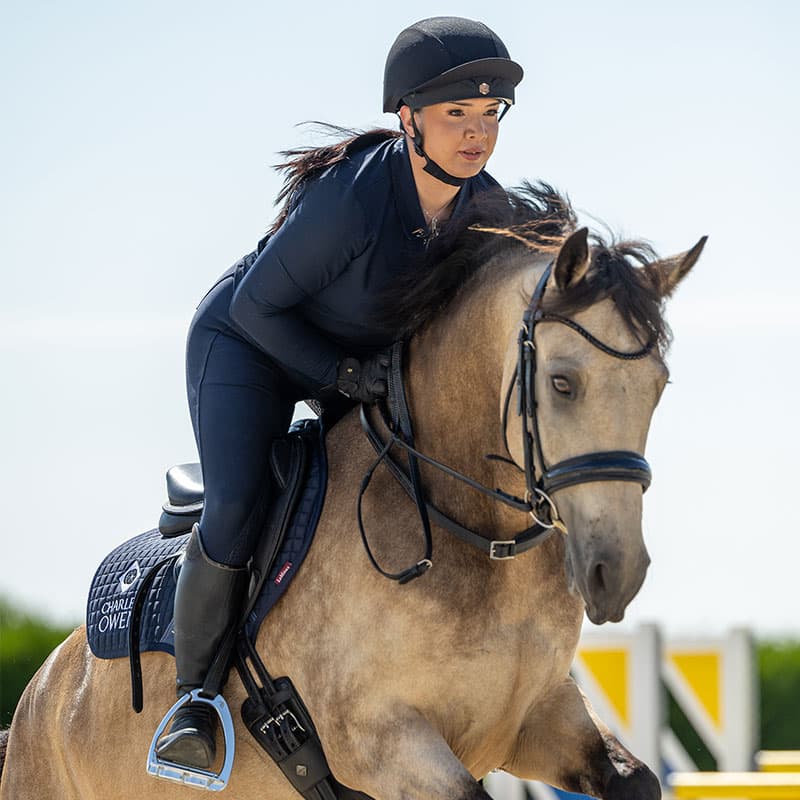 Equestrian: Woman riding horse wearing a Charles Owen riding helmet. Horseback riding safety.