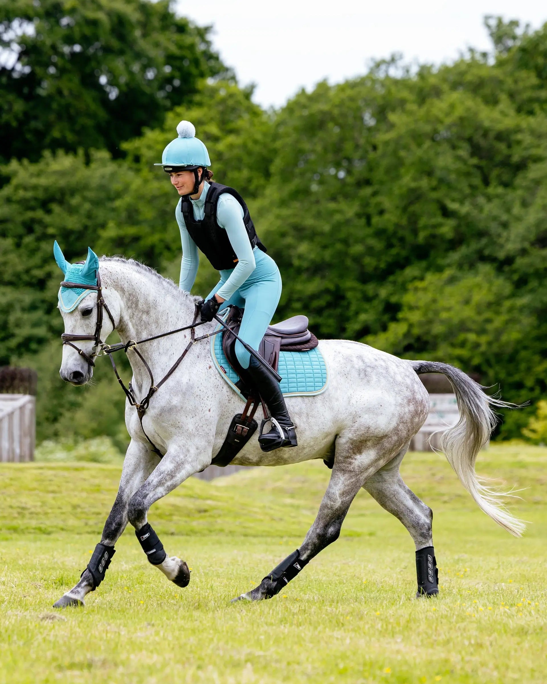 Gray horse with teal LeMieux Suede Close Contact Square Lagoon saddle pad and rider in teal performing equestrian activities.
