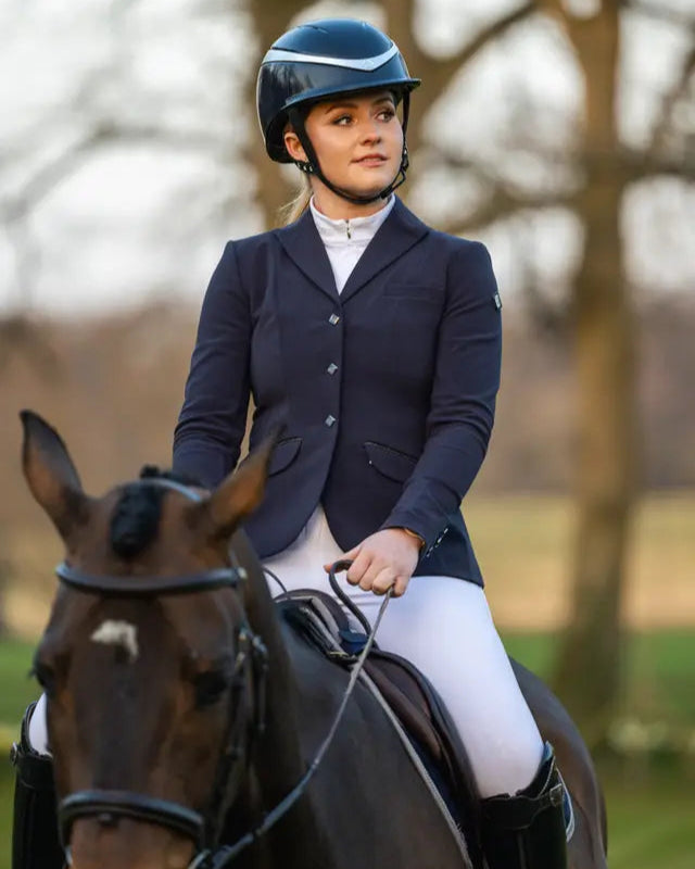 Equestrian woman in LEMIEUX DYNAMIQUE NAVY Show Jacket riding horse. Showjumping competition attire from Equiflair Saddlery