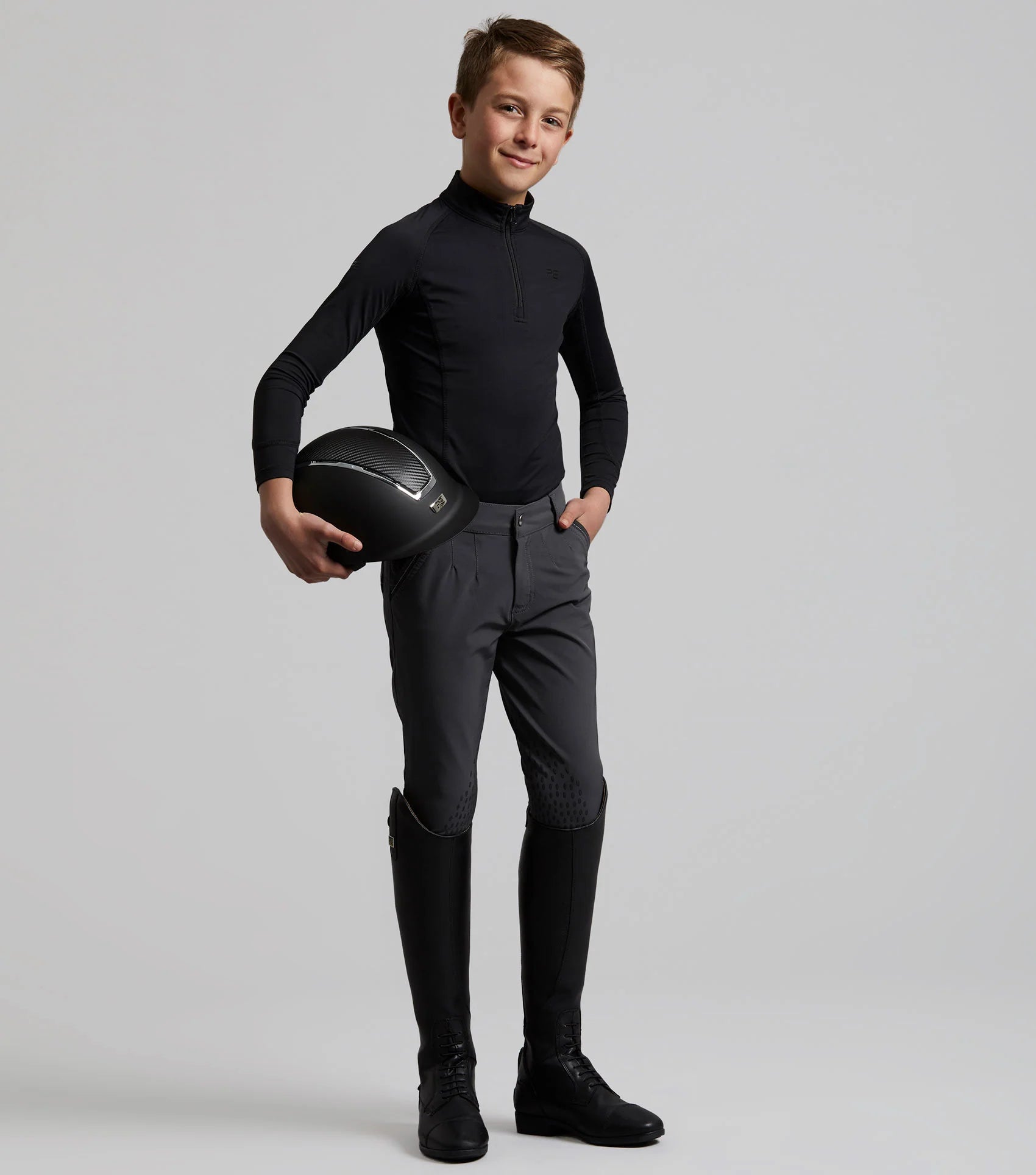 Premier Equine Boys Riding Breeches - Gel Knee, Anthracite Grey. Young equestrian with riding helmet, ready for the arena.