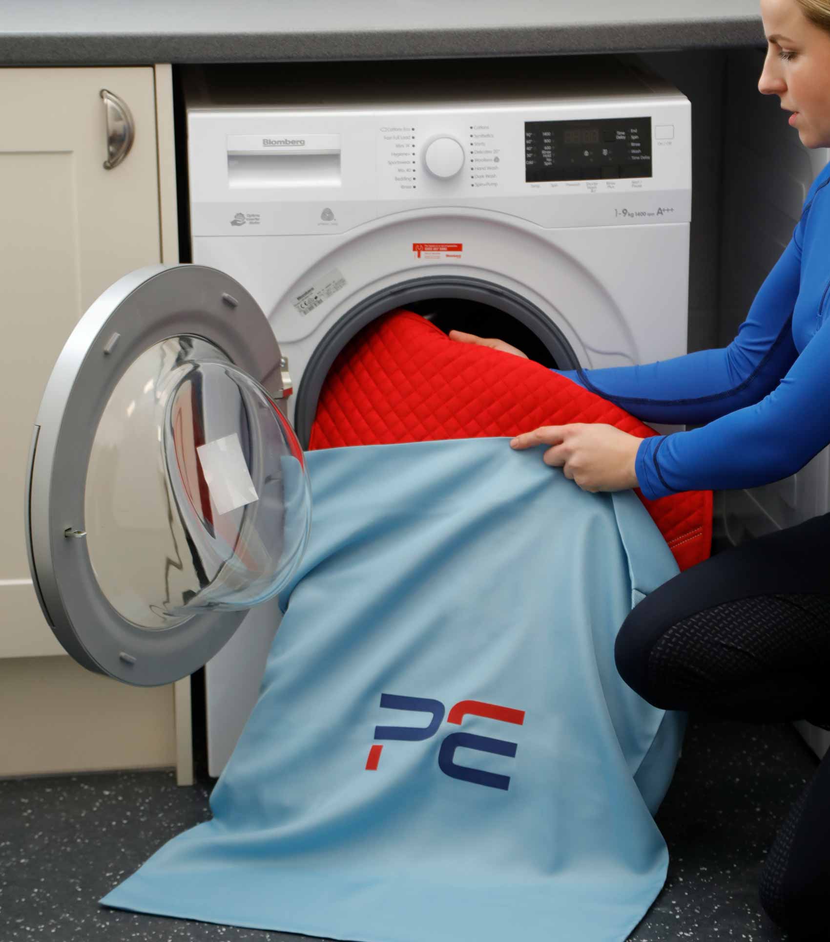 Premier Equine Horse Laundry Wash Bag being loaded into washing machine by woman, product from Equiflair.