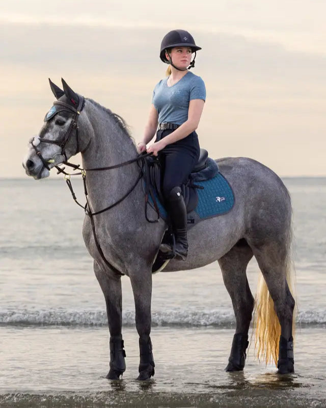 Equestrian Rider on Grey Horse at Beach Wearing LEMIEUX EARTH FLY HOOD OCEAN. Recycled Material Fly Mask for Horses.