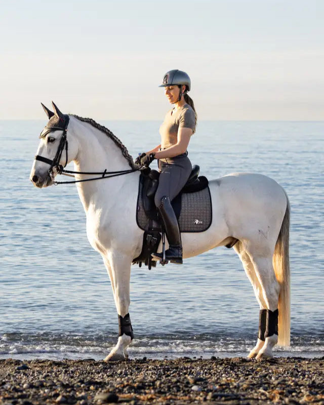 Equiflair: Woman riding white horse on beach with LEMIEUX EARTH DRESSAGE SQUARE MOSS saddle pad.
