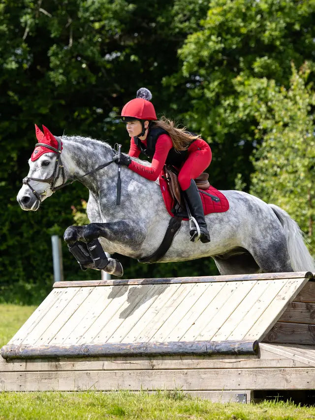 Young equestrian rider in red Lemieux breeches show jumping a grey horse. Children's horse riding gear.