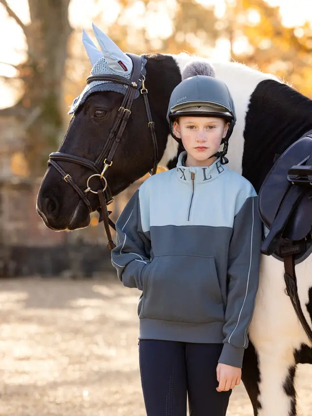 Young rider with horse wearing LeMieux quarter zip sweatshirt and ear bonnet. Equestrian apparel, LeMieux fashion.