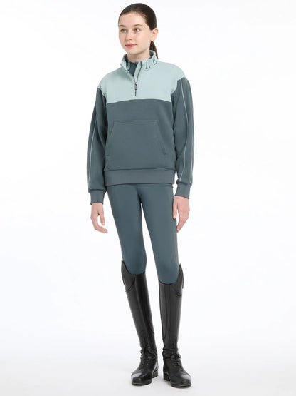 LeMieux Young Rider Kate Quarter Zip Sweat Petrol/Glacier Equestrian Apparel. Young female rider in black boots. 