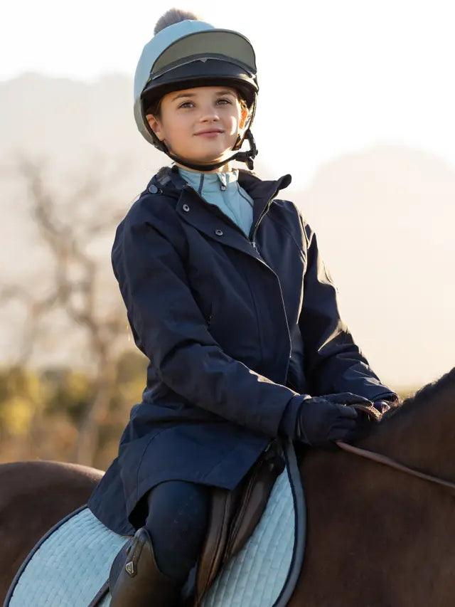 Young girl riding horse wearing Lemieux coat: Equestrian wear, navy waterproof jacket.