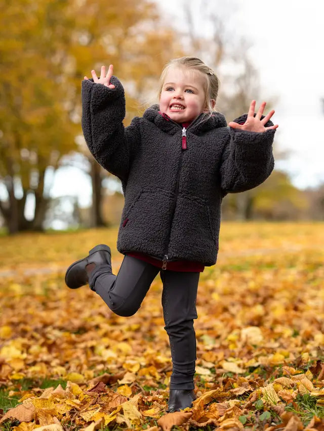 Girl playing in autumn leaves wearing a LeMieux winter coat. Fall fashion, children's clothing, outdoor fun, LeMieux kids.