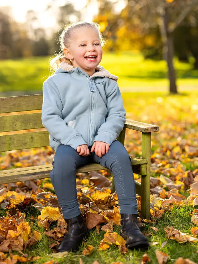 Girl in LEMIEUX Mini Charlie Lined Hoodie Glacier enjoying Autumn outdoor fun. Kids equestrian fashion, comfy hoodie.