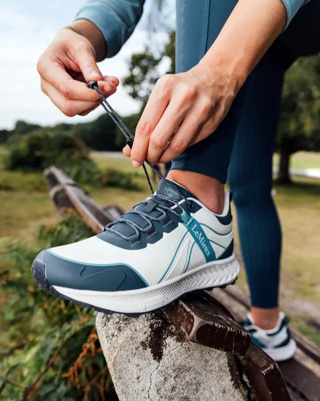 Lemieux Trax 2.0 Waterproof Trainers in Petrol/Ecru being laced up. Equestrian & Active Lifestyle Shoes. Waterproof Outdoor Footwear.