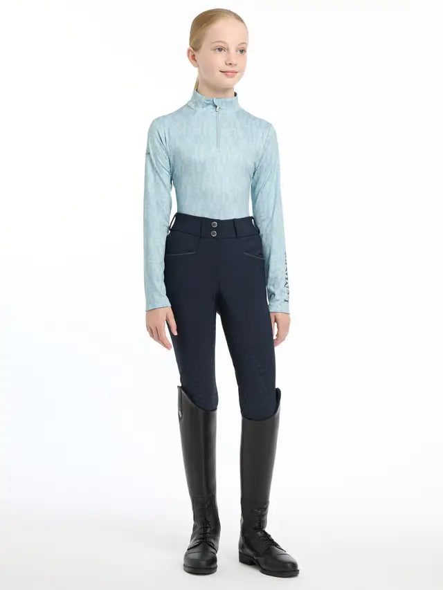 LEMIEUX Young Rider Casey Glacier Base Layer. Girl in riding attire: long-sleeved top, breeches, & boots.