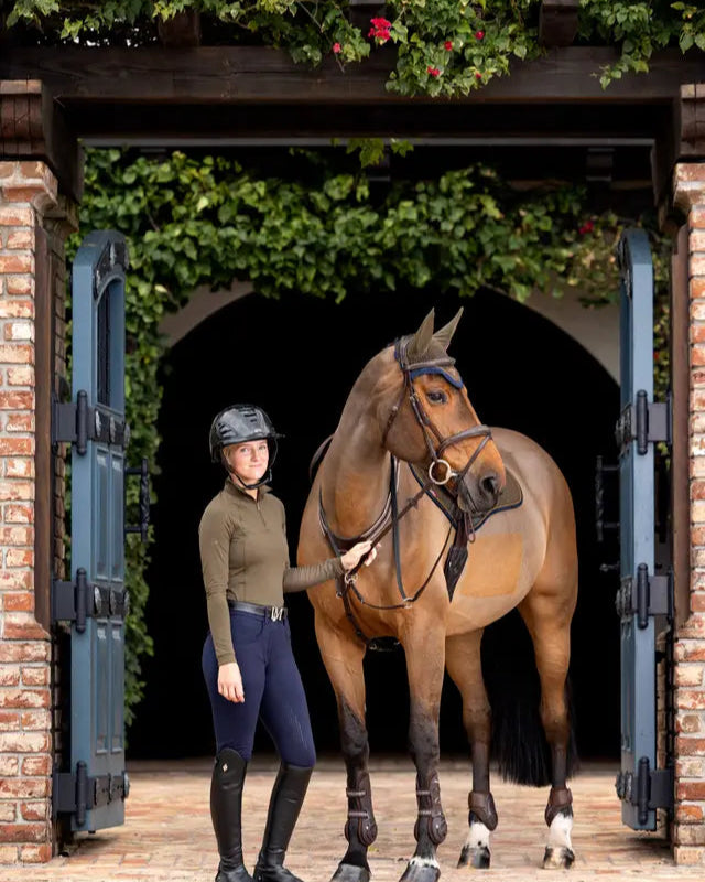 Equestrian outfit: LeMieux Halle Alpine base layer, riding pants, boots, with horse. Lightweight, UV protection for horse riding.