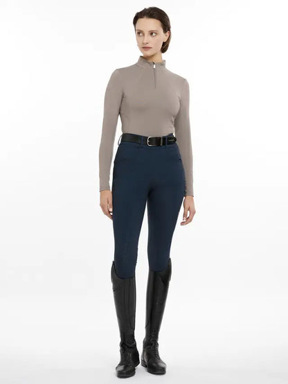 Woman wearing LeMieux Base Layer in Pecan with navy breeches and riding boots. Equestrian clothing and apparel for female riders.