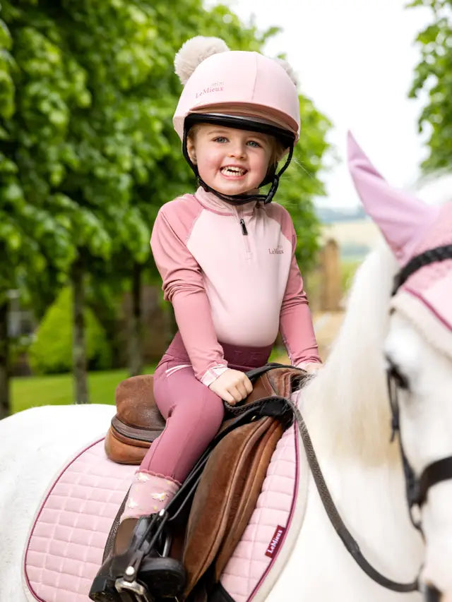 LeMieux Mini Double Pom Hat: A cute child in pink horse riding helmet on white pony. Equestrian style, Equiflair store.