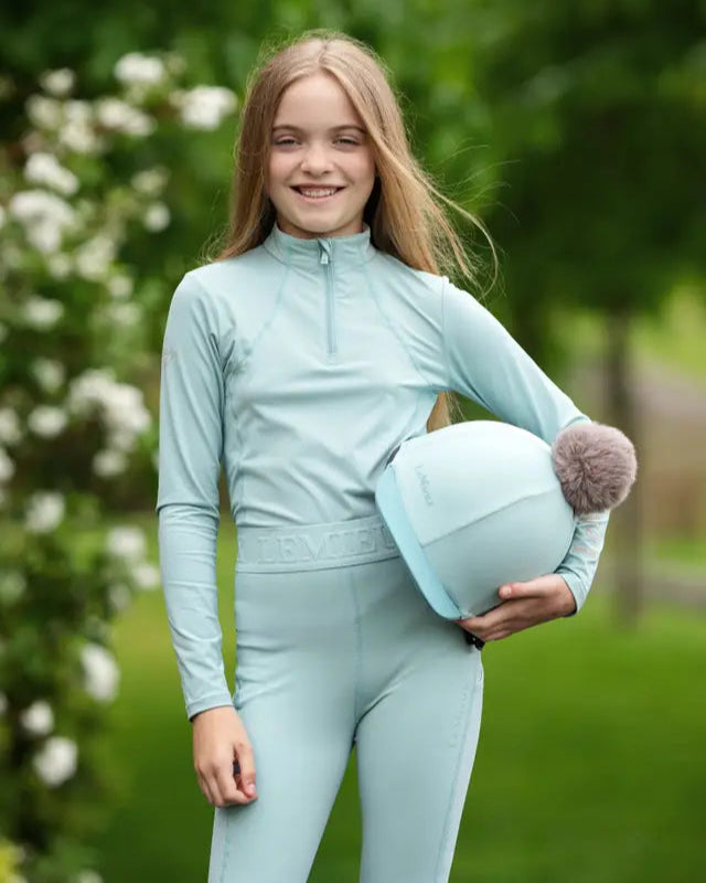 LEMIEUX Pom Hat Silk Aqua/Lagoon at Equiflair: Equestrian riding helmet cover with detachable faux fur pom pom for stylish riders.
