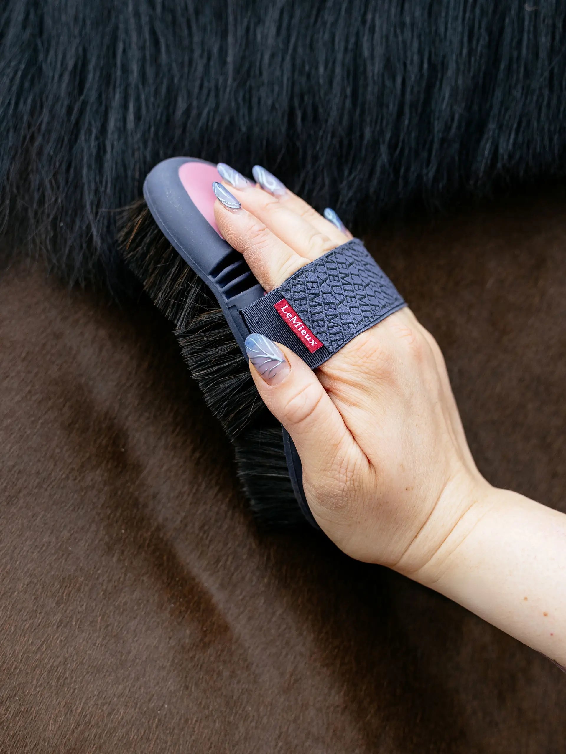 LeMieux Flexi Body Brush Peony: Horse grooming with soft hair brush for sensitive skin. Hand holding brush, close-up.