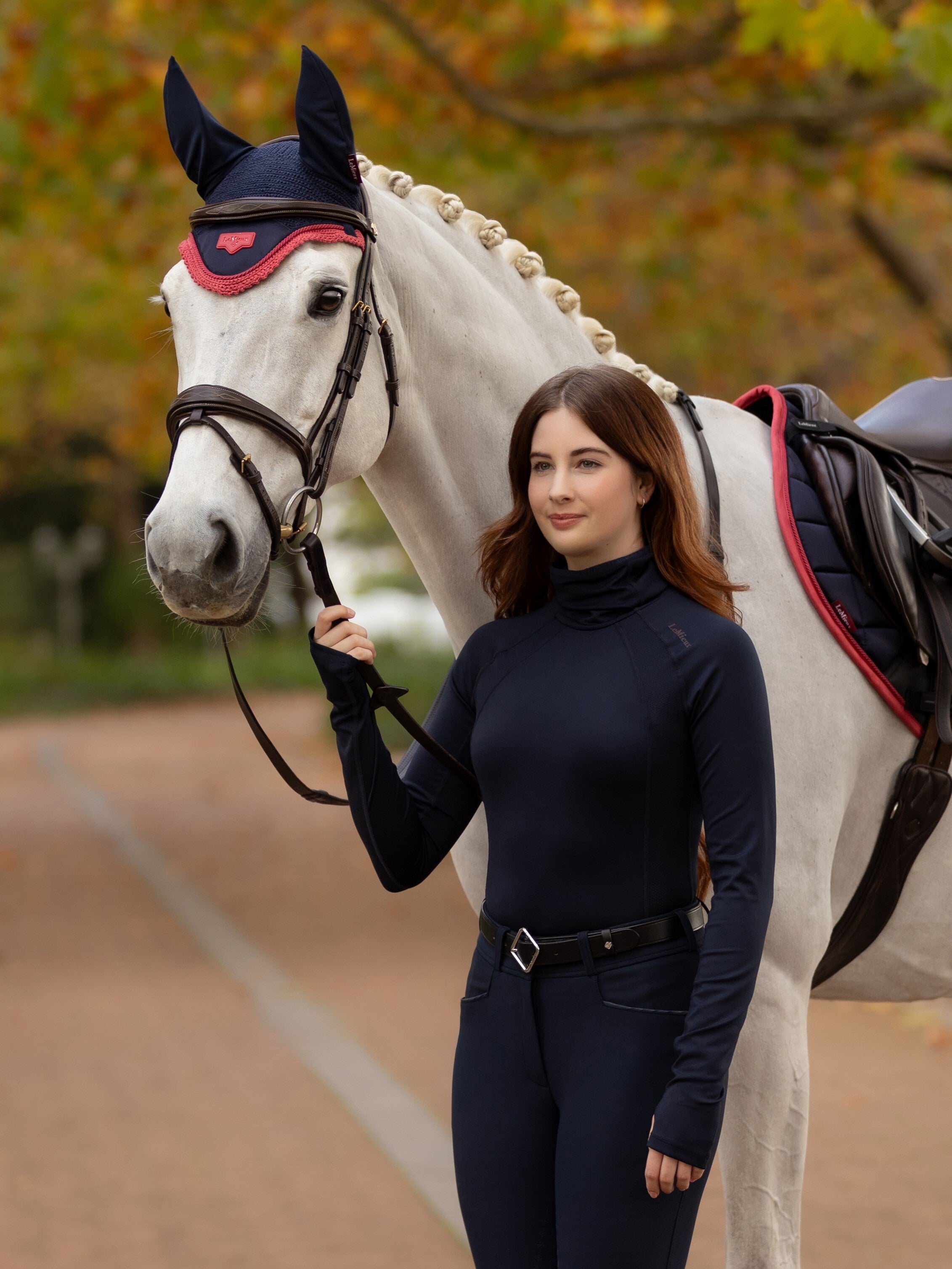LEMIEUX SARA SNOOD BASE LAYER NAVY: Equestrian Apparel for Riding. Woman with horse in LeMieux riding clothes.