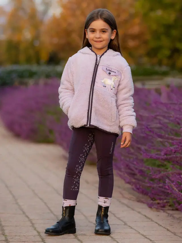 Girl in Lemieux riding gear: purple riding leggings, zipped lavender jacket, equestrian apparel, riding outfit.