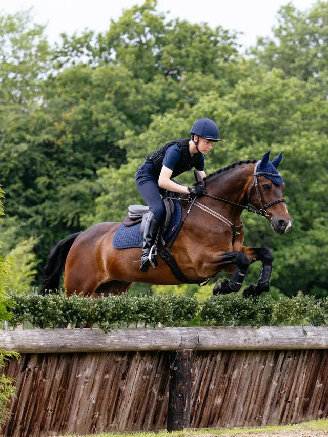 Horse jumping fence with rider in LeMieux gear, equestrian event. LeMieux Cotton Close Contact Square Navy pad. #horsejumping #equestrian