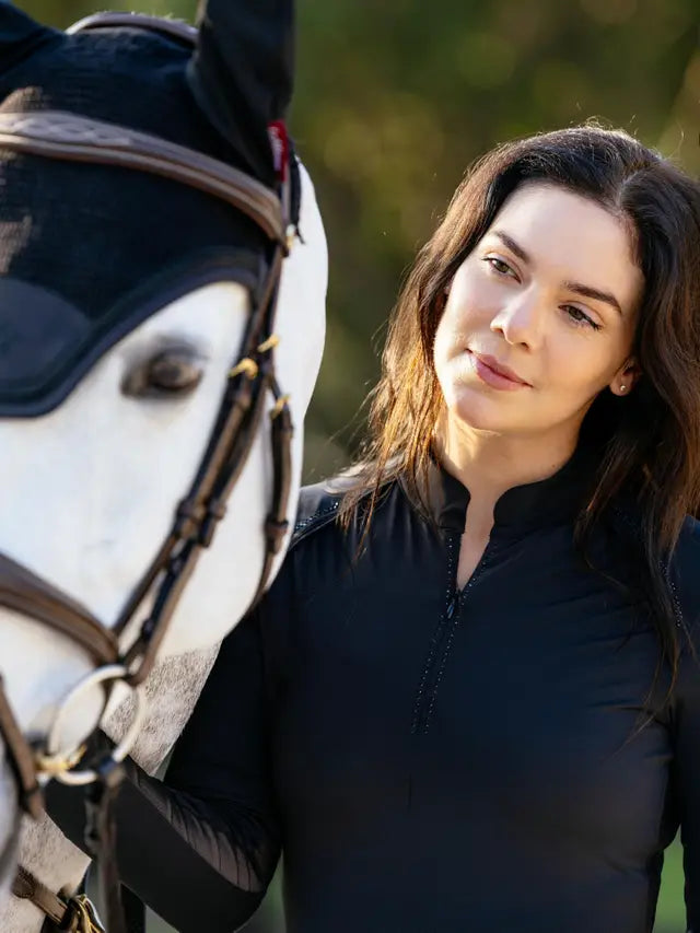 Woman in black LeMieux Brilliance Heyden equestrian base layer with horse, featuring rhinestone details.