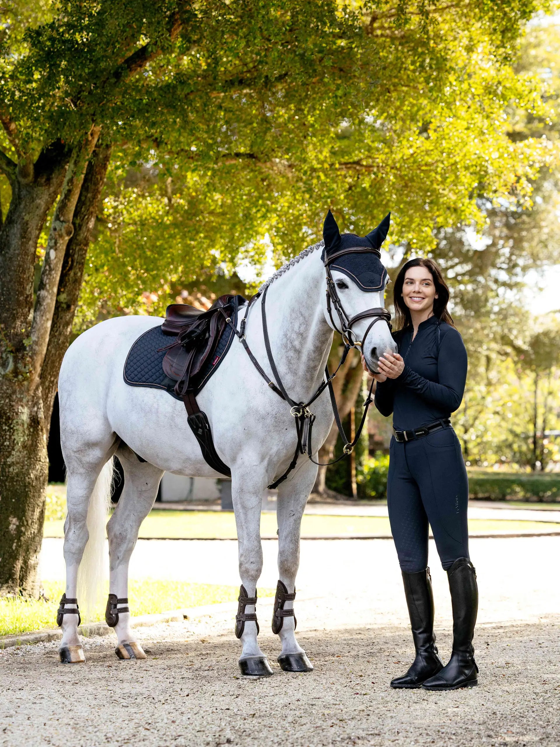 Woman in navy riding outfit with dappled grey horse wearing LeMieux Brilliance Close Contact Square Saddle Pad Navy