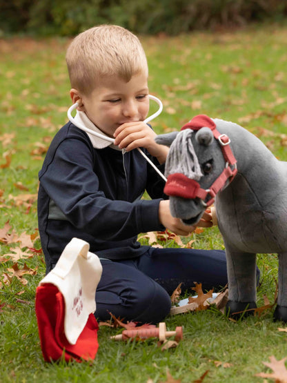 Boy playing with LEMI EUX toy horse vet set outdoors, using stethoscope on toy pony.
