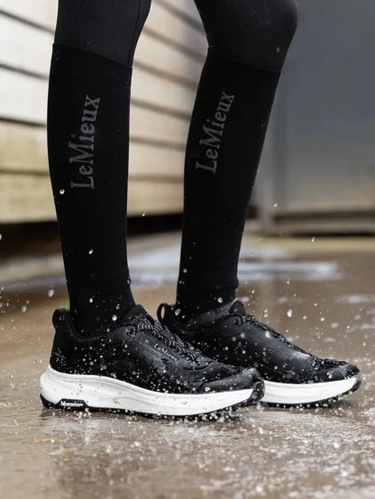 LeMieux Junior Kanta black waterproof trainers with white sole on wet ground.