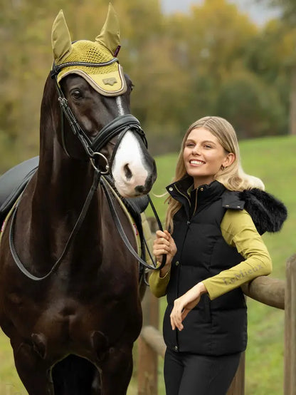 Woman in LeMieux black gilet with horse wearing yellow fly bonnet outdoors