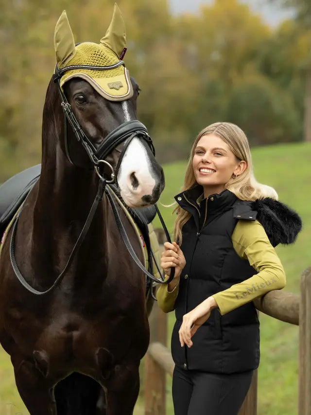 Woman in LeMieux black gilet with horse wearing yellow fly bonnet outdoors