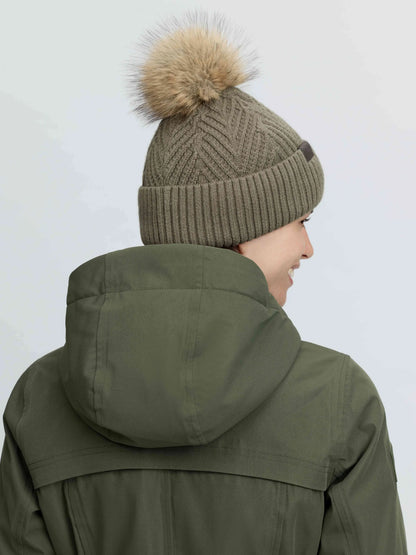 Green LeMieux Clara knit beanie with a fluffy pom-pom, worn with a green jacket.