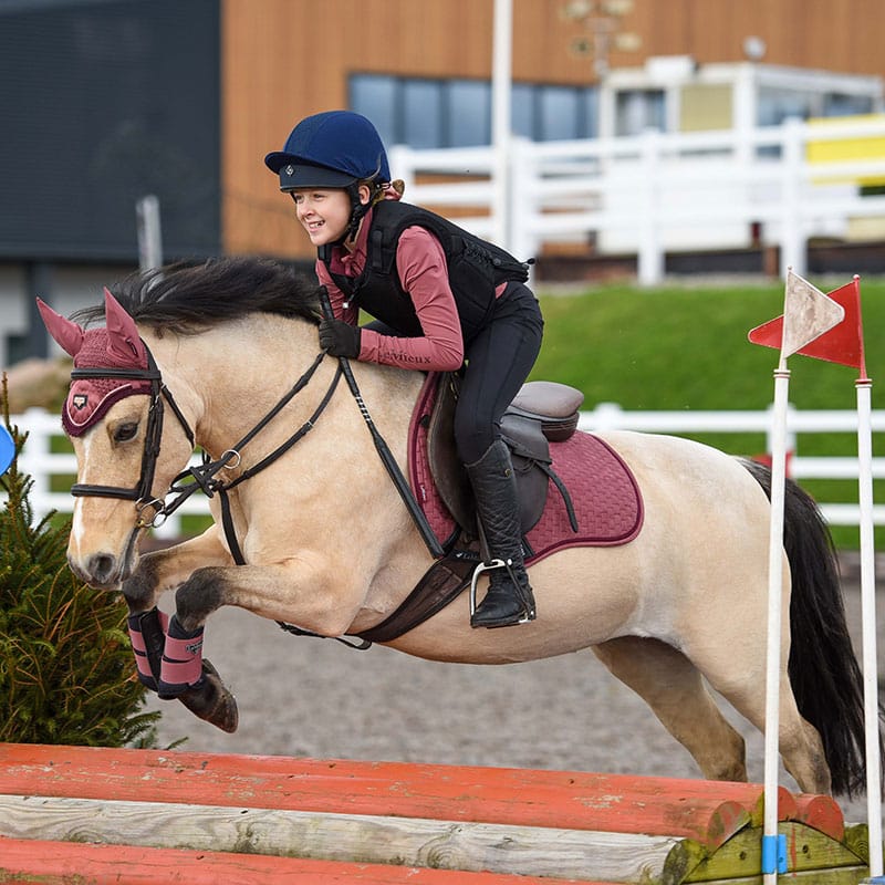 Child equestrian rider in Charles Owen Kontor body protector jumping horse. Equestrian safety wear. Horse jumping, riding equipment.