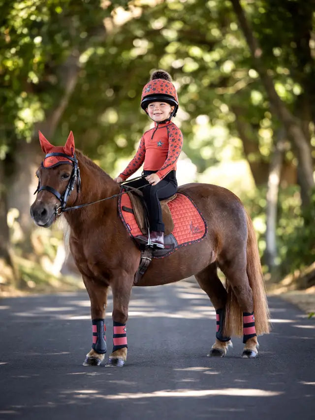 Child on pony wearing matching LEMIEUX Sienna base layer, helmet, and horse riding accessories from Equiflair.