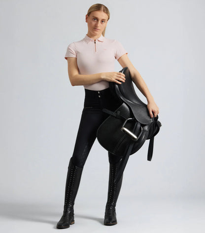 Woman wearing black Premier Equine riding breeches with full seat holding a horse saddle. Equestrian fashion.