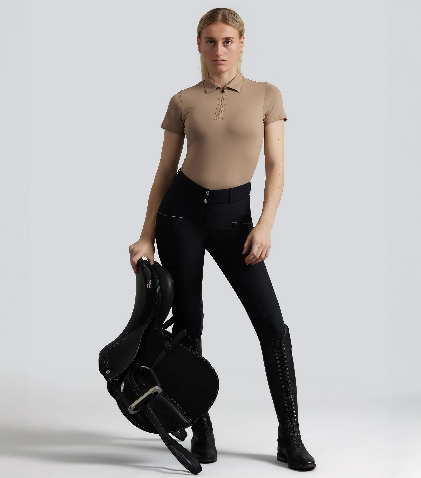Equestrian rider in black riding breeches holding saddle. Gel knee breeches and riding boots. #riding #equestrian
