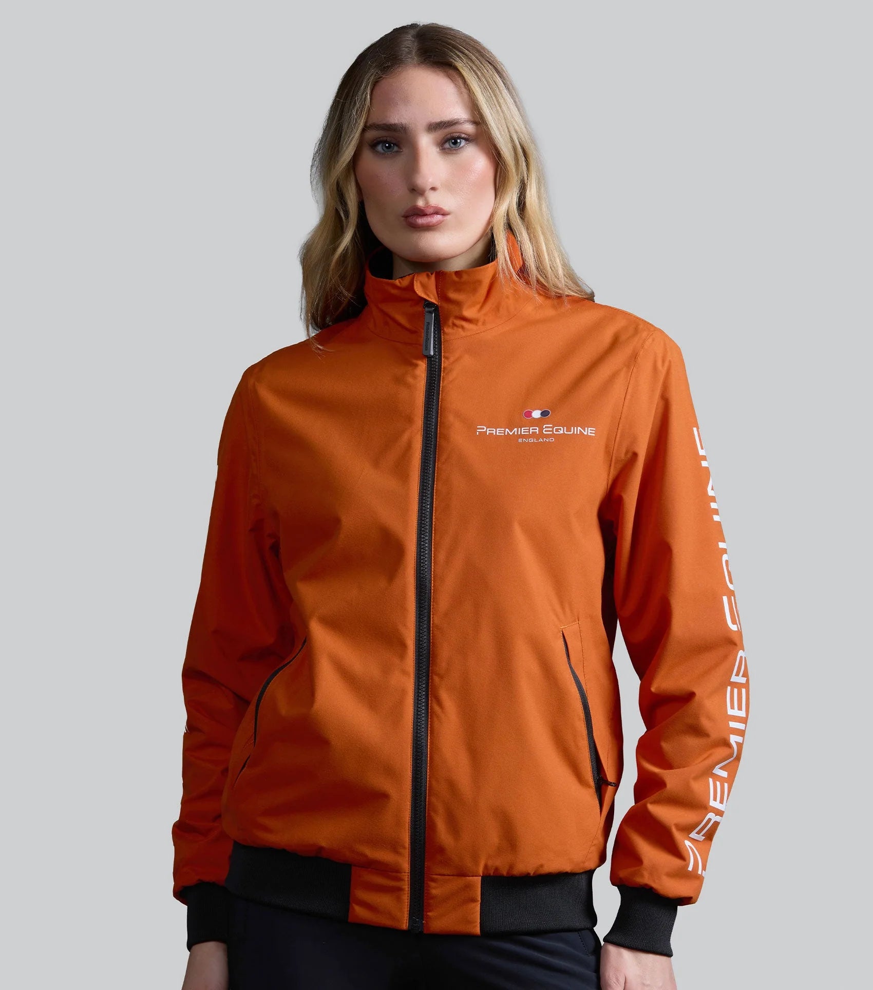 Premier Equine Women's Waterproof Riding Jacket - Burnt Orange. Woman wearing horse riding apparel by Equiflair store.