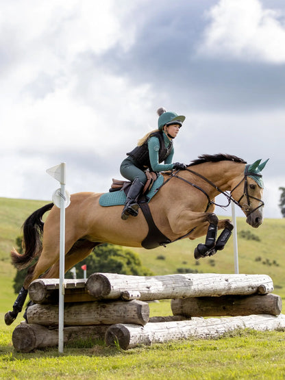 Equestrian: Horse jumping over logs. Rider in LEMIEUX Sage hat silk by Equiflair. Horse eventing action shot.