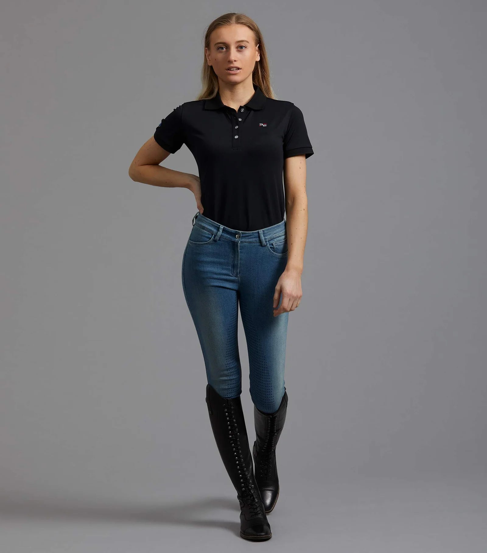 Woman in black equestrian polo shirt, blue riding jeans, and black riding boots.