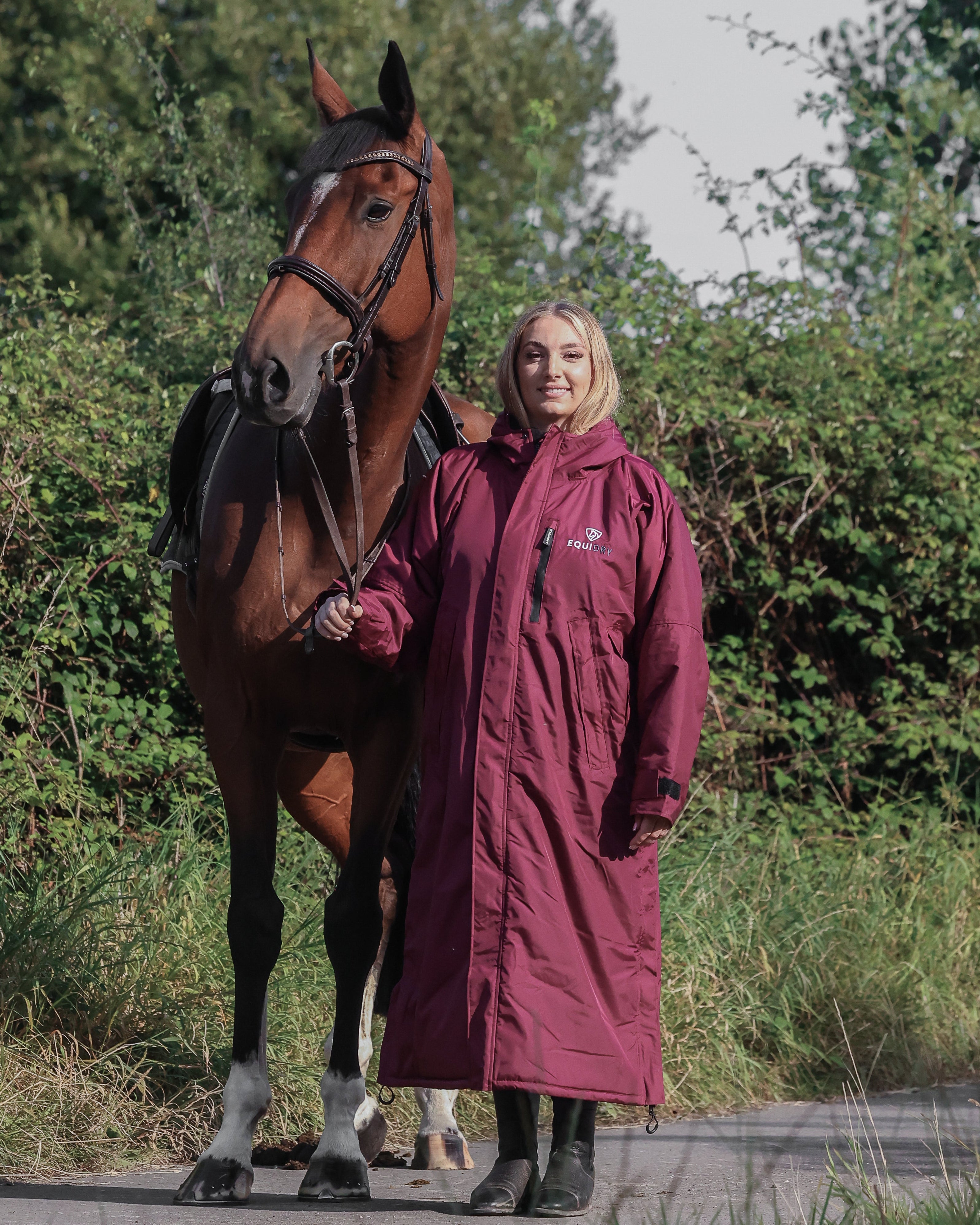 Woman with horse wearing EQUIDRY Plum Riding Coat. Waterproof equestrian apparel.