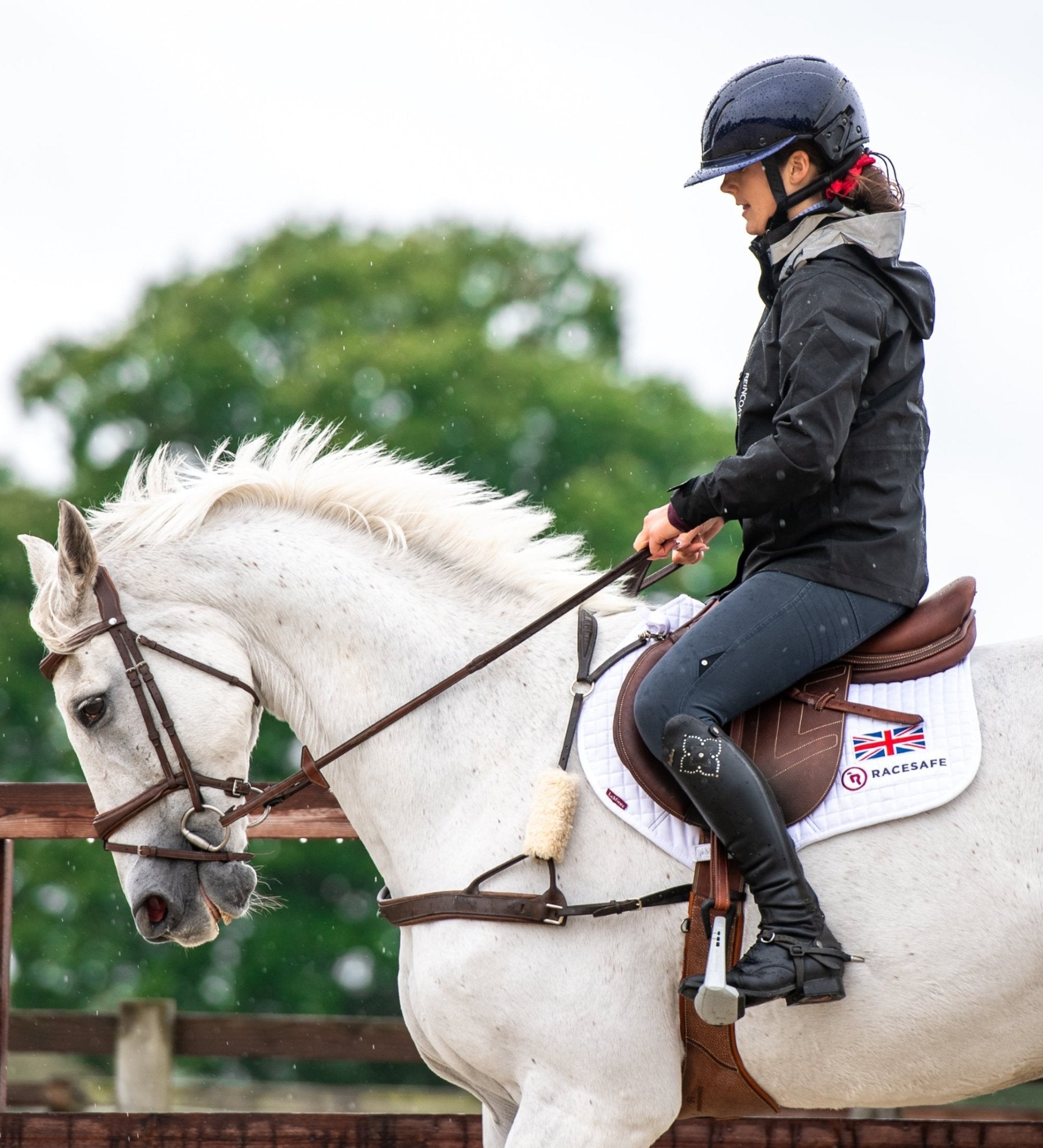 Equestrian rider in Reincoat waterproof jacket on horse with Racesafe saddle pad. Horse riding in UK.