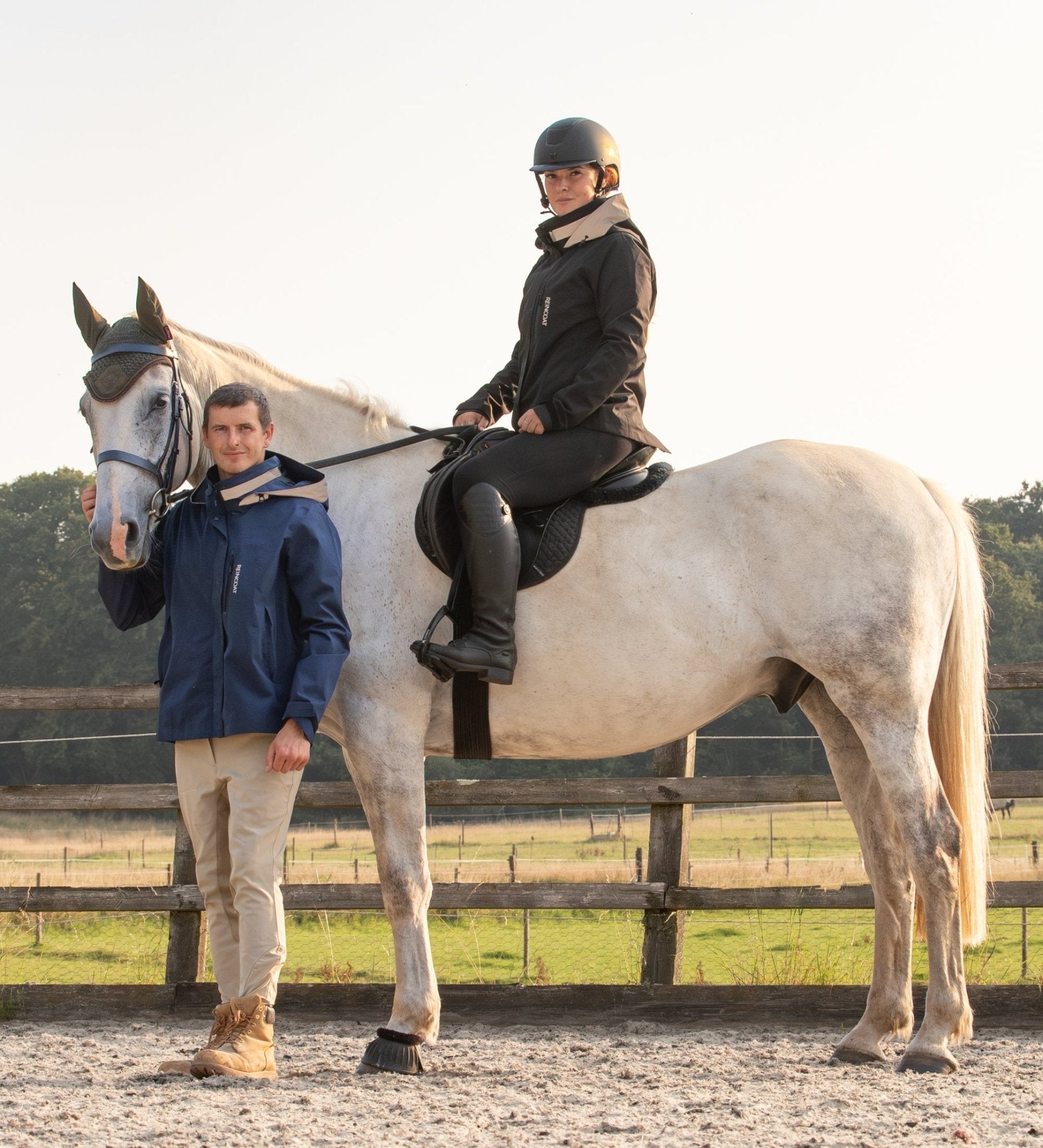 Equestrian: Reincoat Air Adult - Midnight Navy Waterproof Jacket. Woman on horse with trainer in riding coat.