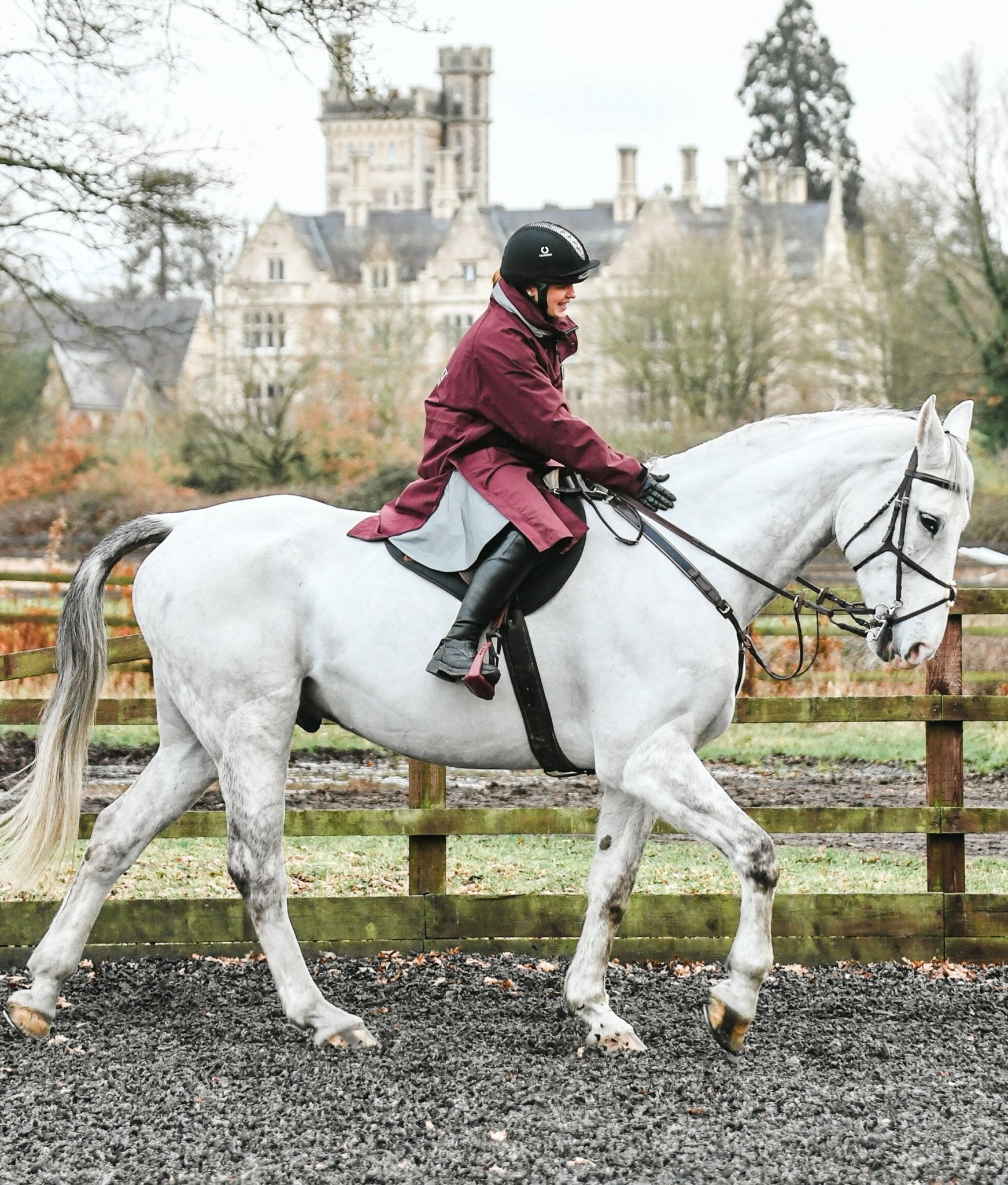 Equestrian in Burgundy Equiflair Reincoat riding Grey Horse near Castle. Horse Riding, Dressage. Reflective Reincoat.