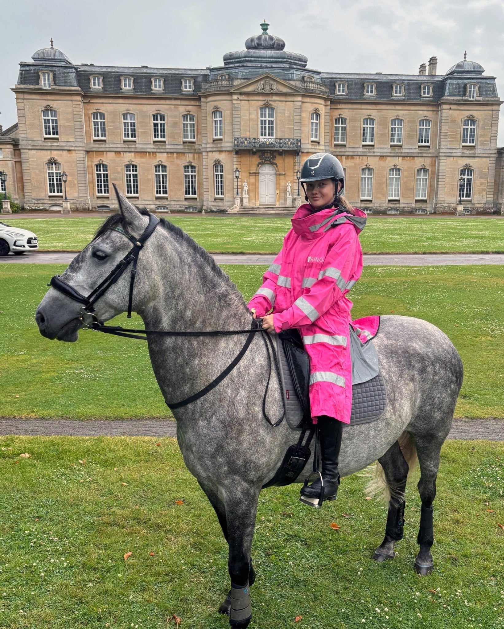Reincoat Lite Adult - Hi-Vis Pink. Woman riding horse in Equiflair waterproof jacket, reflective for safety. Horse riding gear.