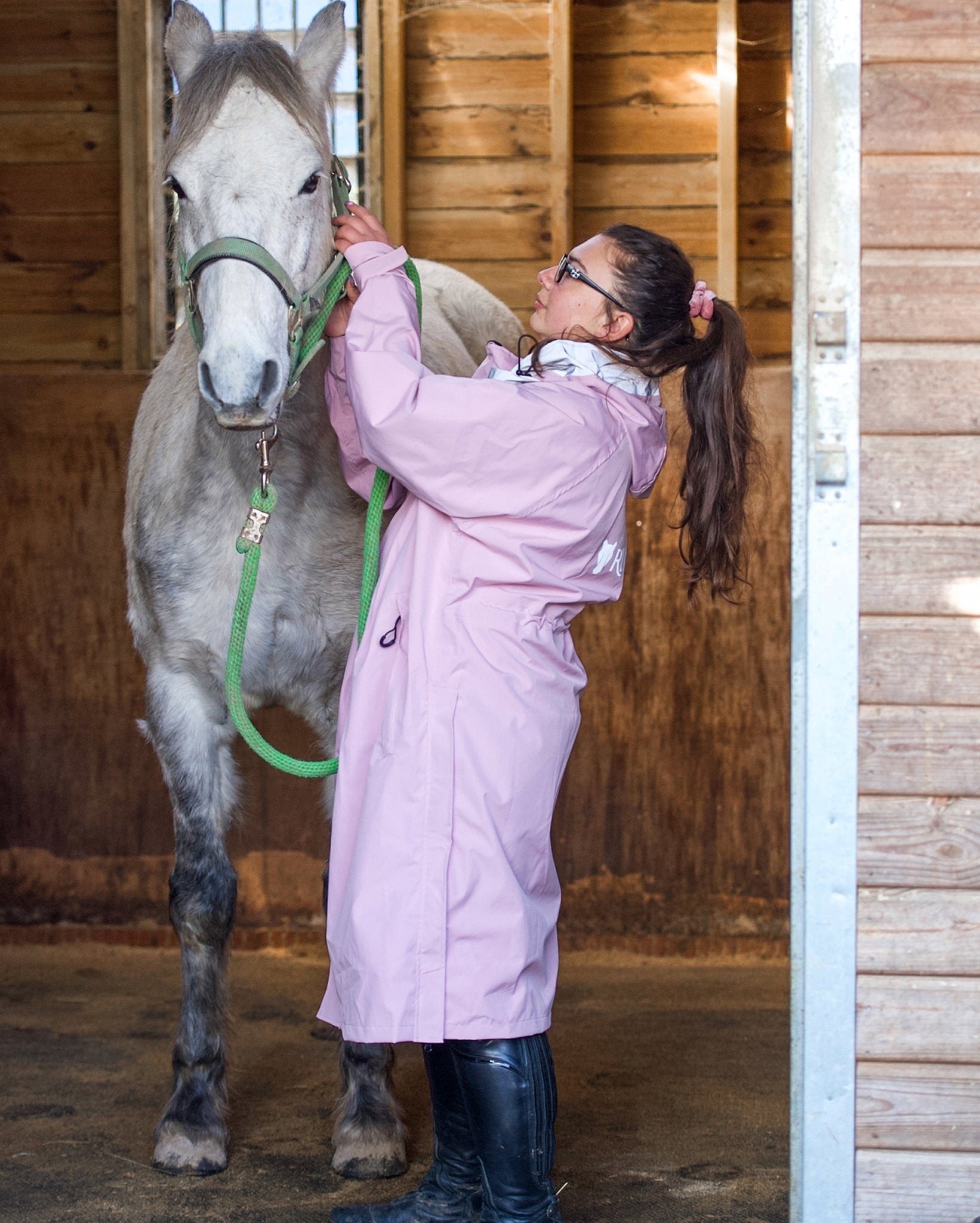 Woman in Equiflair Pink Raincoat with Horse in Stable | Equestrian Fashion