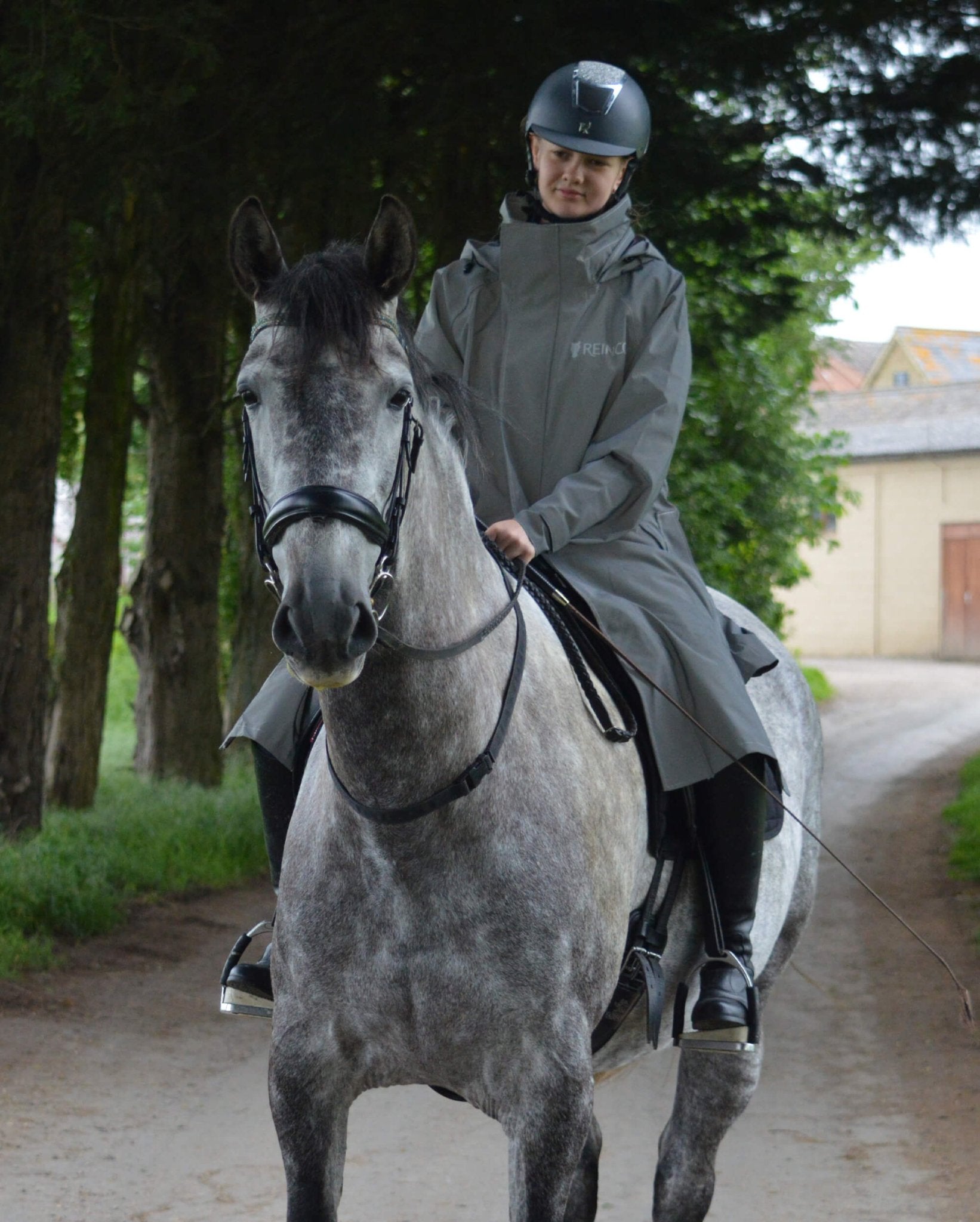 Girl in REINCOAT LITE KIDS reflective horse riding raincoat. Children's waterproof riding jacket with safety reflective silver.