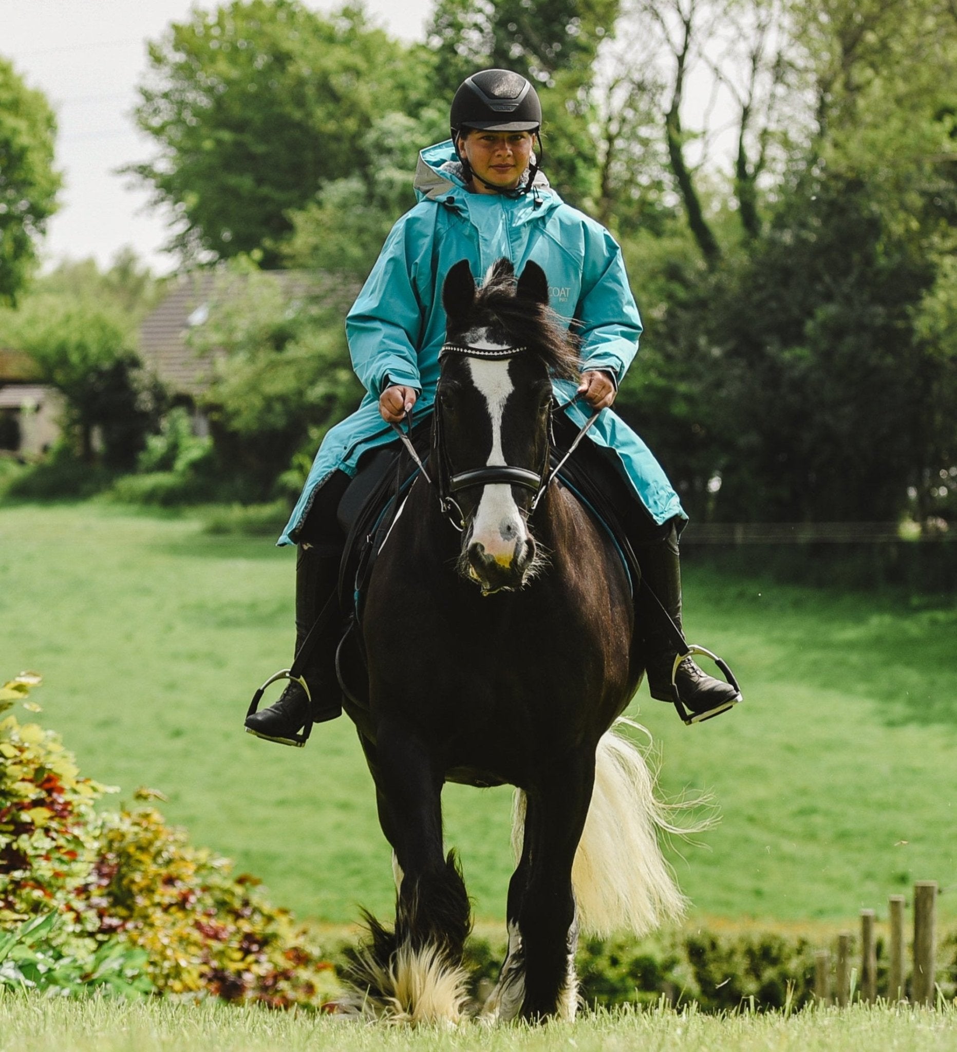 Horseback Riding: Woman Rider in Blue Waterproof Raincoat and Helmet on Horse in Field. Equiflair Gear for Equestrian Sports.