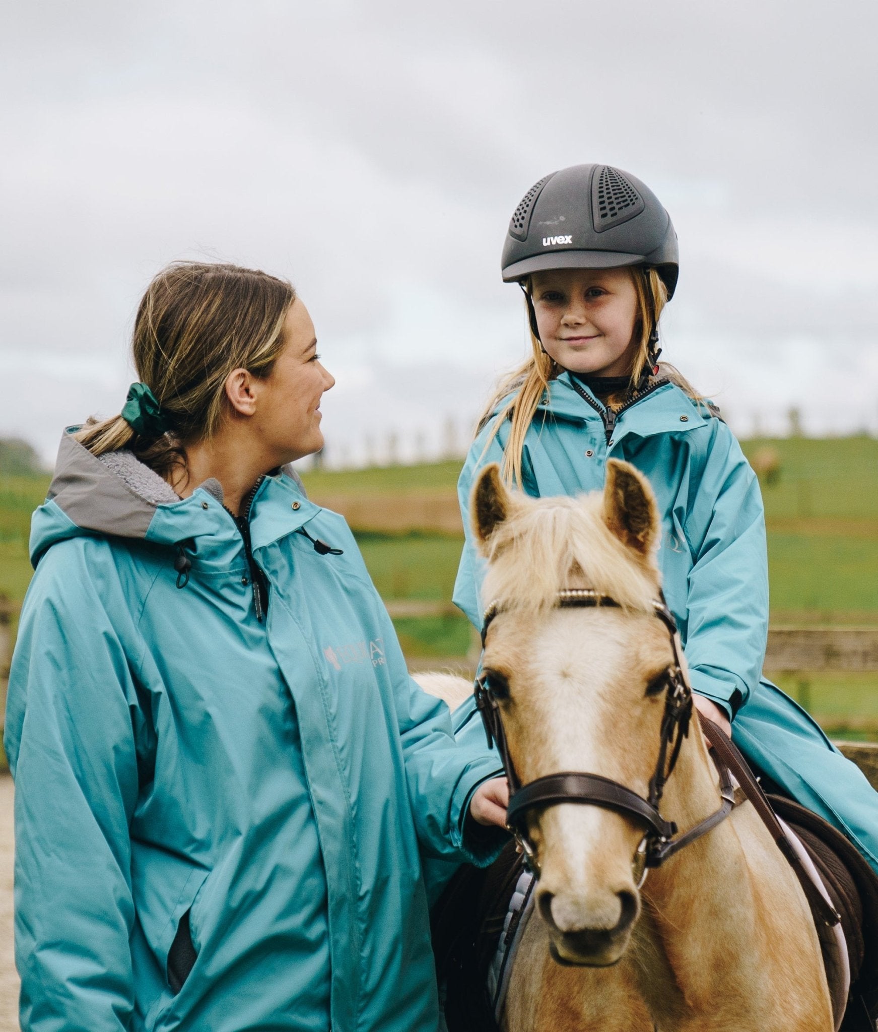 Equiflair's Teal Reincoat Pro Kids: Girl riding pony in waterproof kids riding coat & helmet. Equestrian gear, horseback riding apparel.